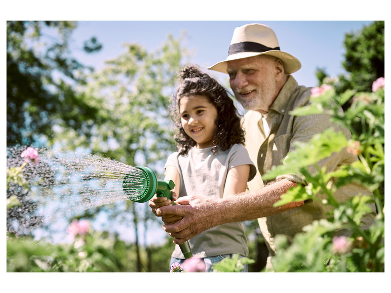 Een man en een meisje besproeien planten in de tuin met een groene gieter.