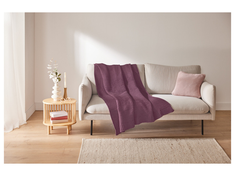 Een paarse wollen deken op een beige bank met een beige vloerkleed.