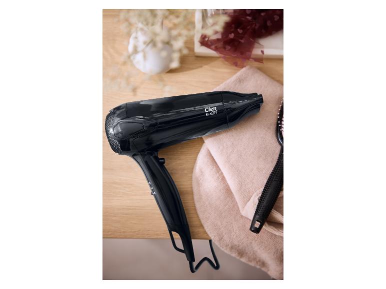 Zwarte Cien Beauty föhn en haarborstel op een houten tafel met een handdoek.