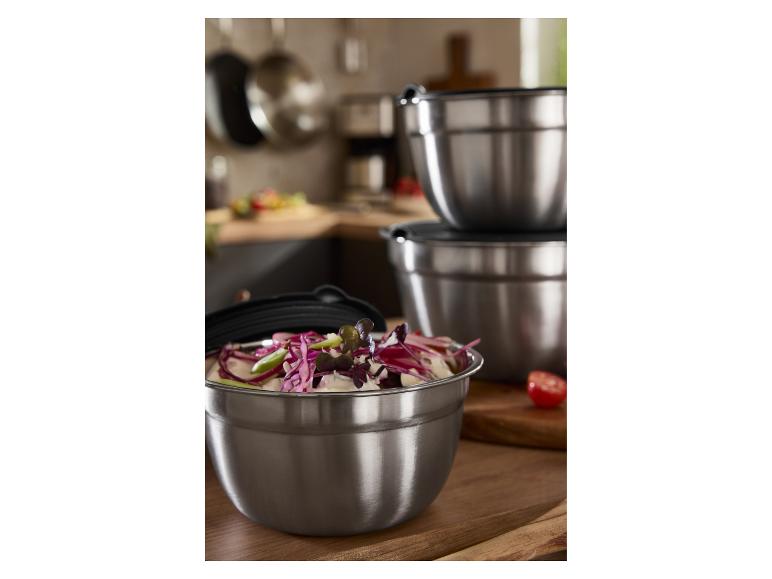 Roestvrijstalen mengkommen met deksels, één gevuld met salade, in een keuken.