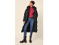 Vrouw in lange zwarte pufferjas, rode coltrui, blauwe jeans en zwarte laarzen.