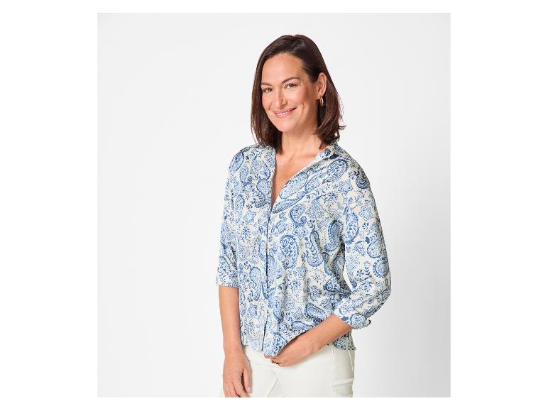 Lachende vrouw met een blauw-wit patroon overhemd en een witte broek.