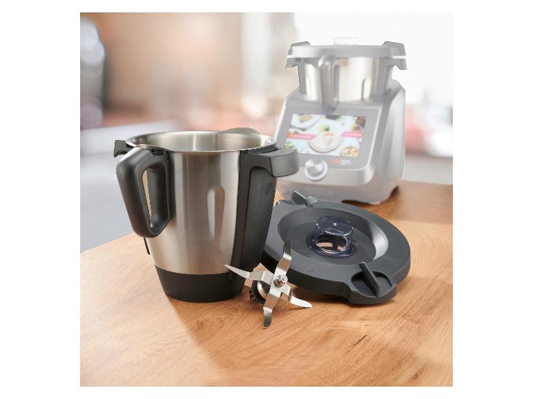 Roestvrijstalen mengkom met messen en deksel, met de keukenmachine op de achtergrond.