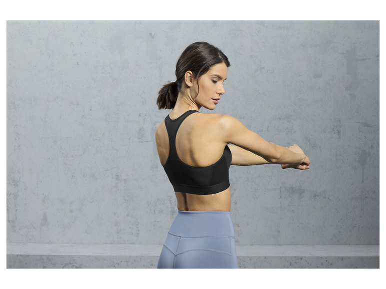 Een vrouw draagt een zwarte sportbeha en blauwe leggings.