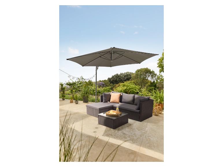 Buiten loungeset van rotan met kussens, glazen salontafel en grote grijze parasol.