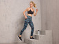 Vrouw in sportbeha en leggings met print, loopt op een betonnen trap.