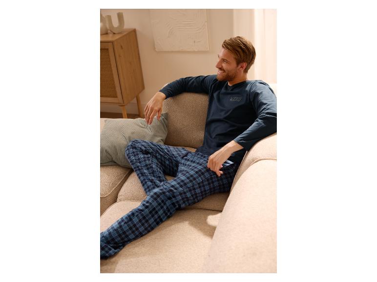 Lachende man in blauw geruite pyjama ontspant op een bank.