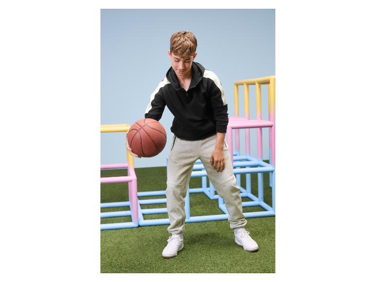 Tiener in grijze joggingbroek en zwarte hoodie met een basketbal