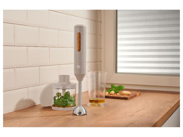 Staafmixer met basilicum, olijfolie en kaas op een houten aanrecht in een keuken.