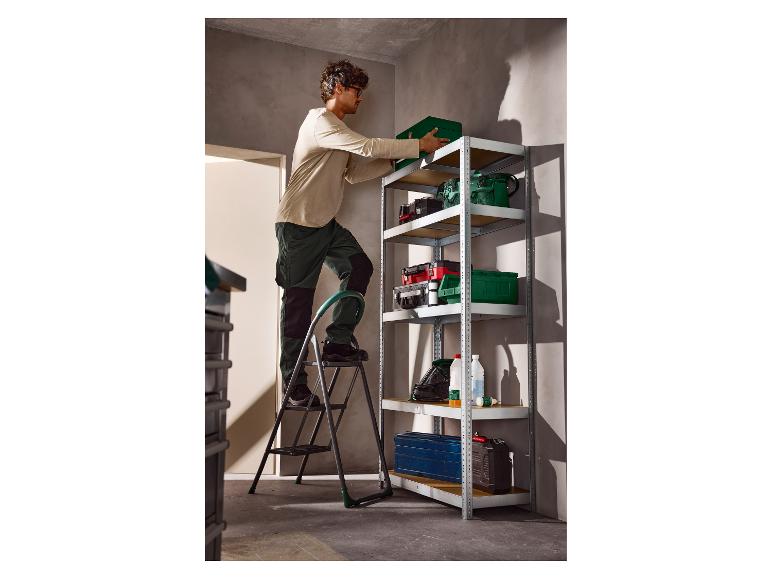 Man op een ladder plaatst een groene doos op een metalen rek met gereedschap.