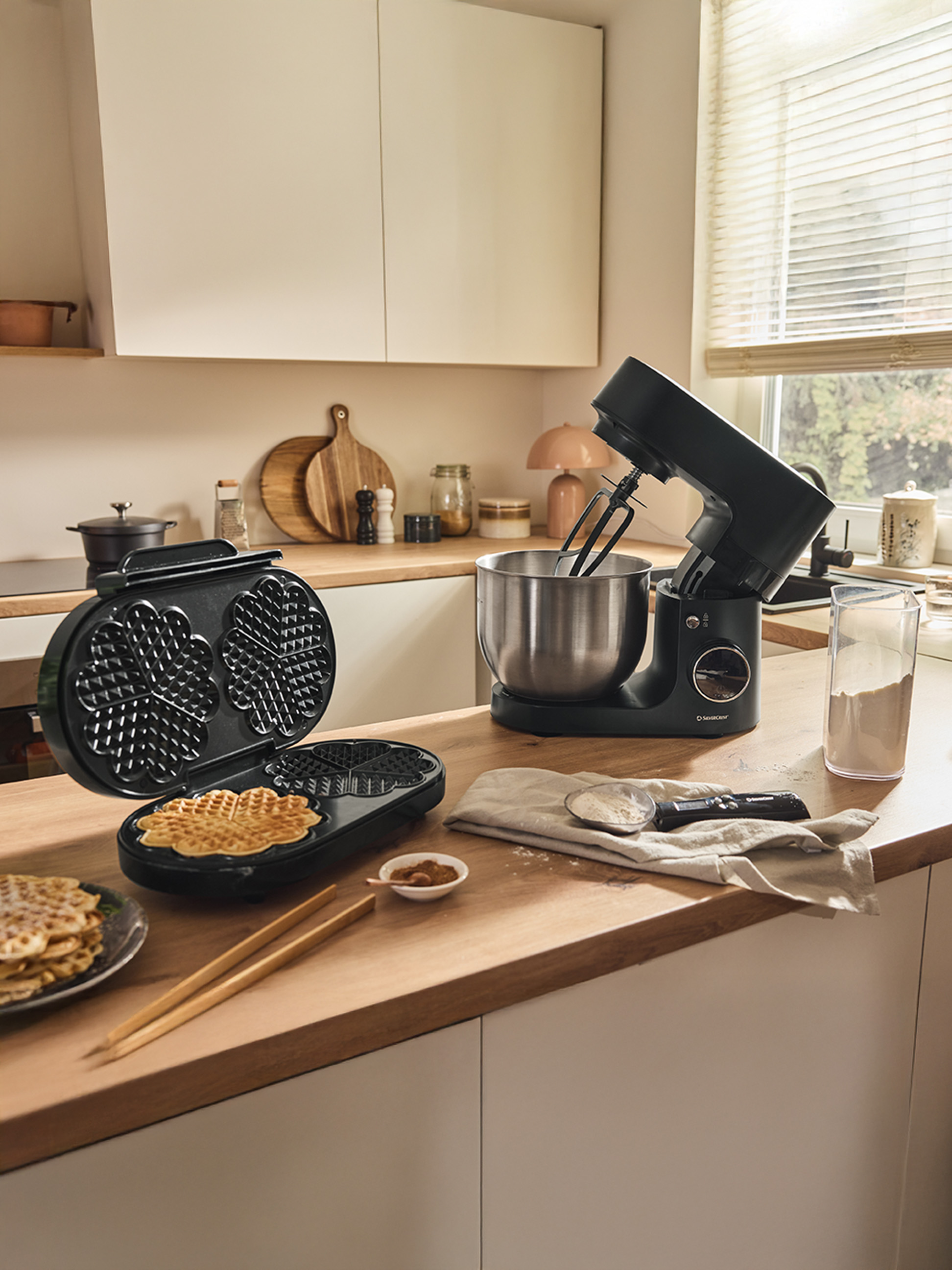 Een wafelijzer en een zwarte keukenmixer op een houten aanrecht, met kant-en-klare wafels.