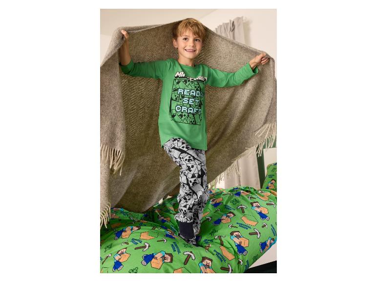 Jongen in groene Minecraft pyjama met 'READ, SET, CRAFT' tekst, staand op een Minecraft dekbed.