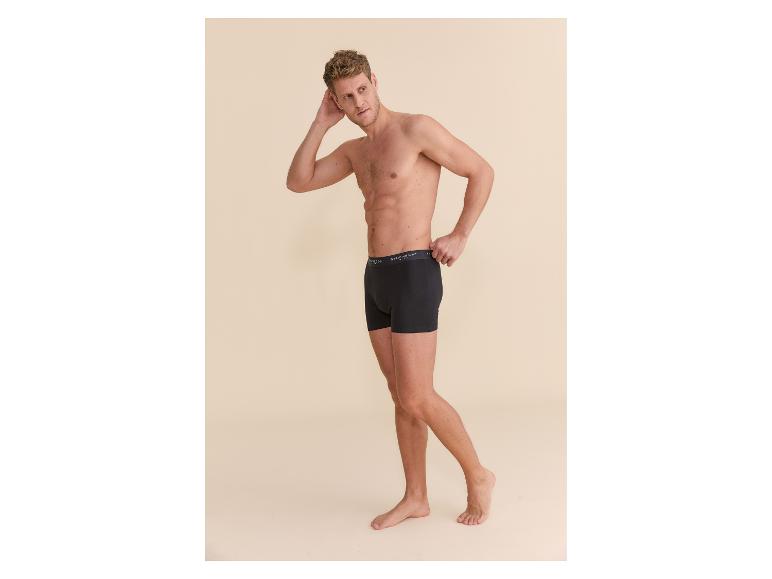 Blonde man in zwarte boxershorts, tegen een beige achtergrond.