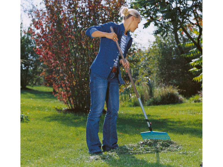 Een vrouw harkt bladeren met een blauwe hark in de tuin.