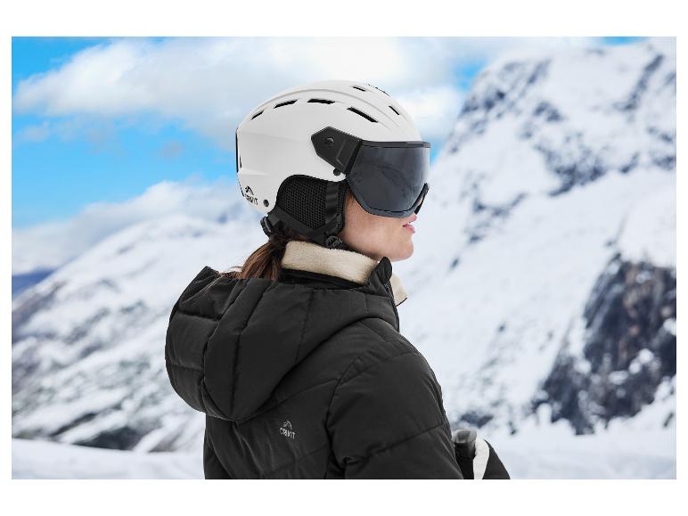 Een persoon in een zwarte ski-jas en witte skihelm met vizier, kijkend naar besneeuwde bergen.