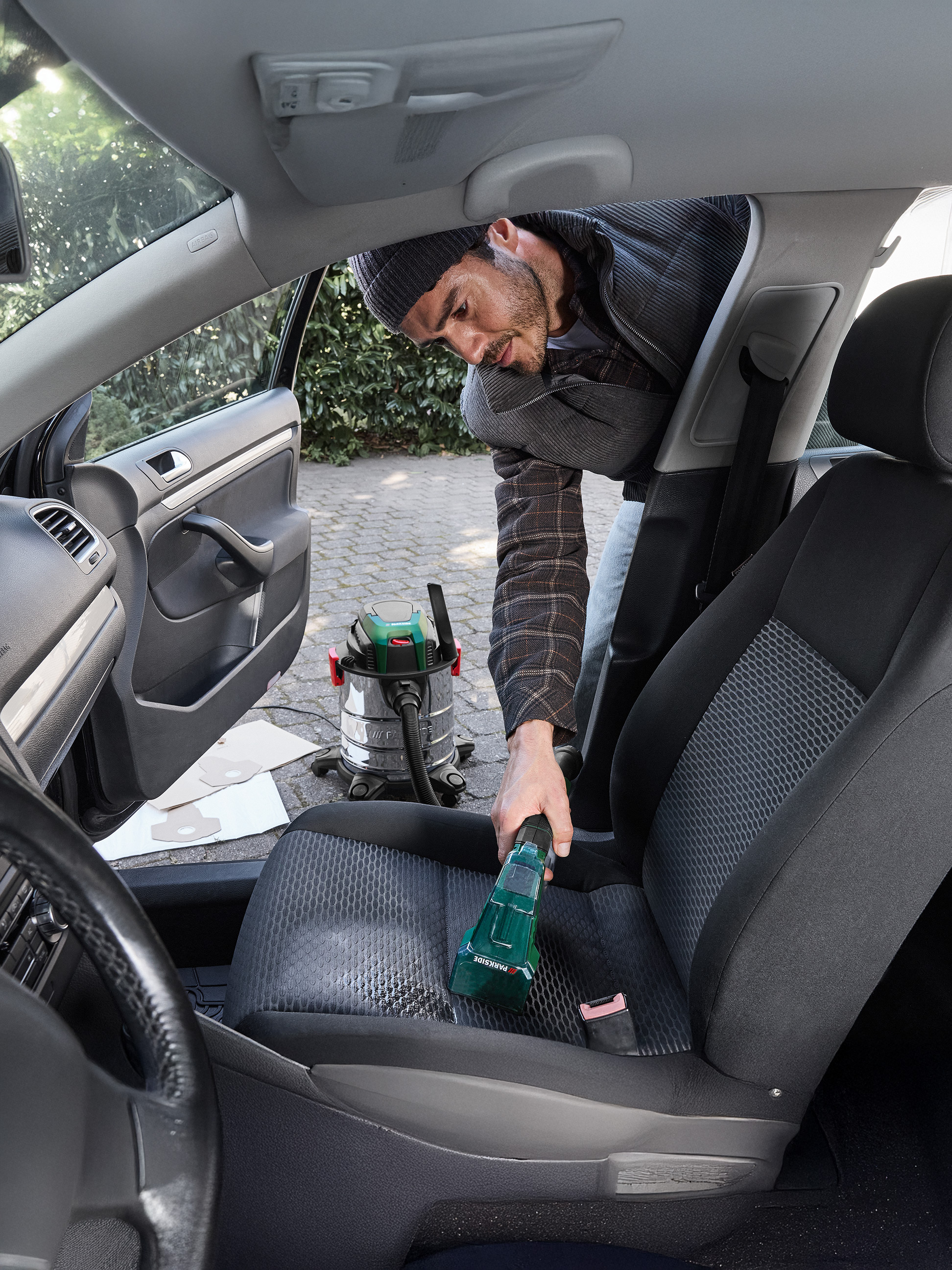 Man reinigt autostoel met Parkside kruimeldief, met een nat-/droogzuiger op de achtergrond.