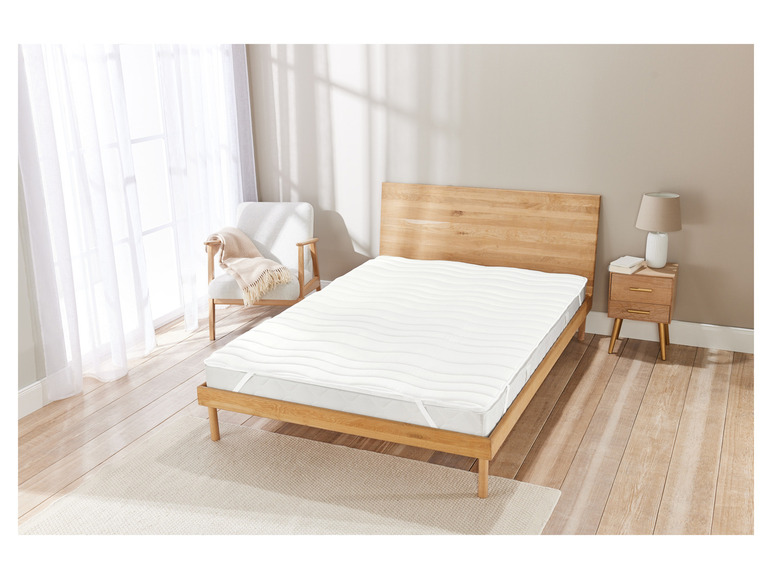 Een wit matrasbeschermer met golvende structuur op een houten bedframe.