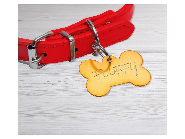 Rode hondenhalsband met een botvormig label gegraveerd met 'FLUFFY' op een houten ondergrond.