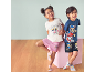 Twee lachende kinderen in zomerpyjama's met puppy-prints, tegen een lichtblauwe achtergrond en houten vloer.