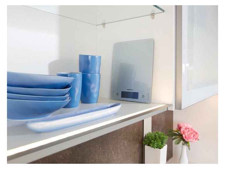Keukenweegschaal en blauw servies op een verlichte plank.