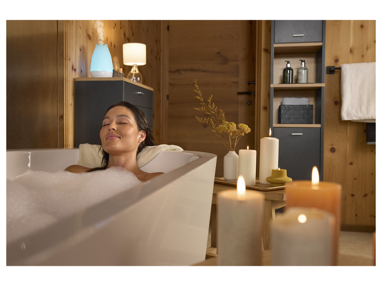 Een vrouw ontspant in een bad met schuim, omringd door kaarsen en een luchtbevochtiger.