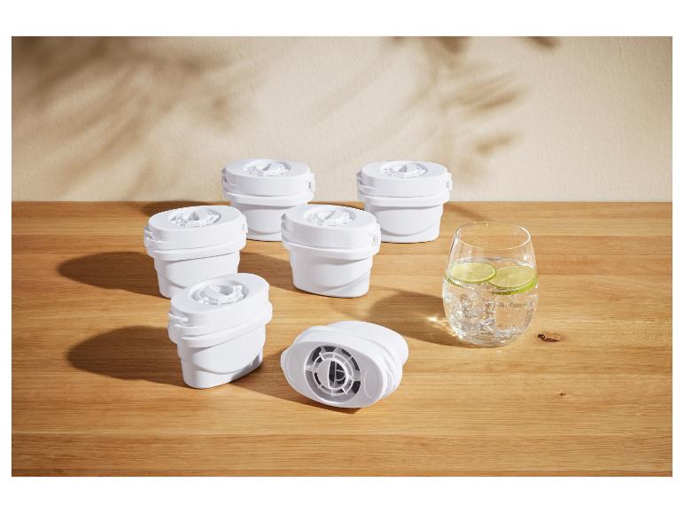 Zes witte waterfilters en een glas water met limoen op een houten tafel.