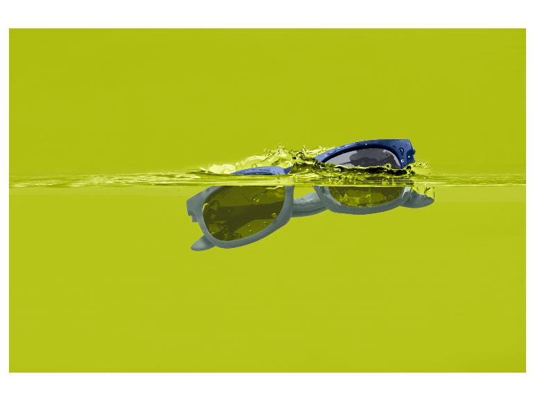 Blauwe zonnebril drijvend in geel water met spetters.