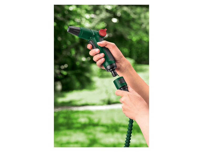 Handen verbinden een groene tuinslang met een groen spuitpistool met een rode knop.