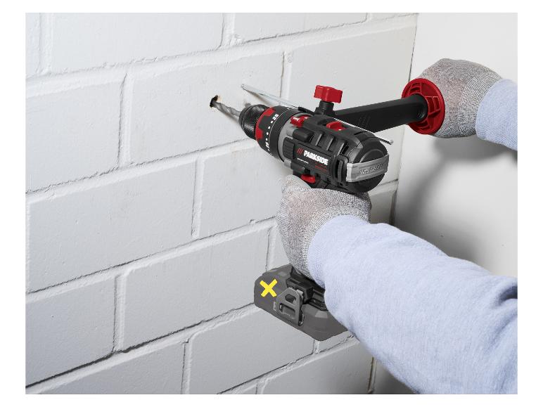 Persoon boort een gat in een witte bakstenen muur met een accuboormachine.