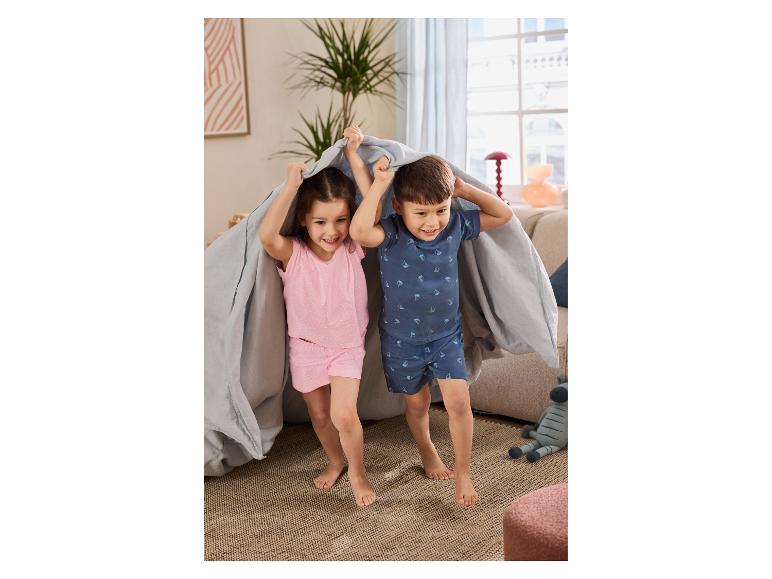 Twee kinderen in zomerpyjama spelen lachend onder een laken.