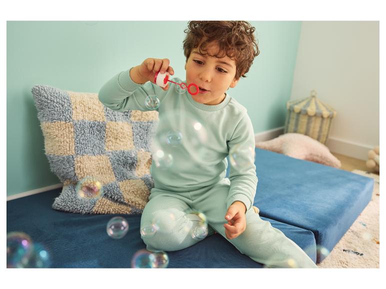 Jongetje in trainingspak blaast bellen op een blauw matras.