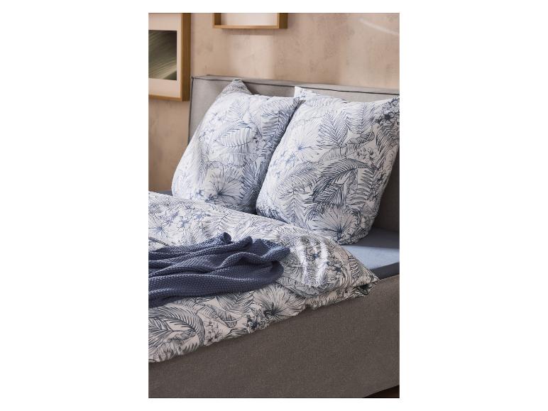 Bed met blauw-wit tropisch bladpatroon dekbedovertrek en kussens, en een blauw gebreide plaid.