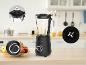 Zwarte blender met glazen kan en appels op een houten tafel in een keuken.