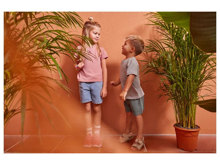 Twee kinderen in casual zomerkleding, een meisje in een roze t-shirt en denim shorts, een jongen in een grijs t-shirt en groene shorts.