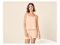 Lachende vrouw in een perzikkleurige tweedelige pyjama met spaghettibandjes top en shorts.