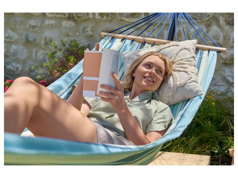 Vrouw ontspant in een hangmat met een boek in de tuin.