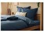 Marineblauwe beddengoed op een houten bed met decoratieve kussens en planten.