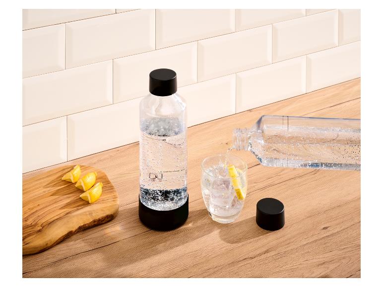 Fles bruiswater en glas met ijs en citroen op een houten aanrecht.