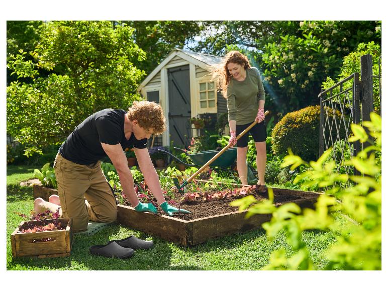 Man en vrouw planten groenten in een verhoogde moestuin, met tuinschoenen en gereedschap.