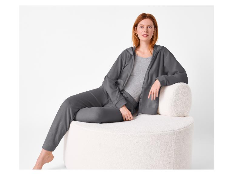 Vrouw in een grijze loungewear set zittend op een witte getextureerde stoel.