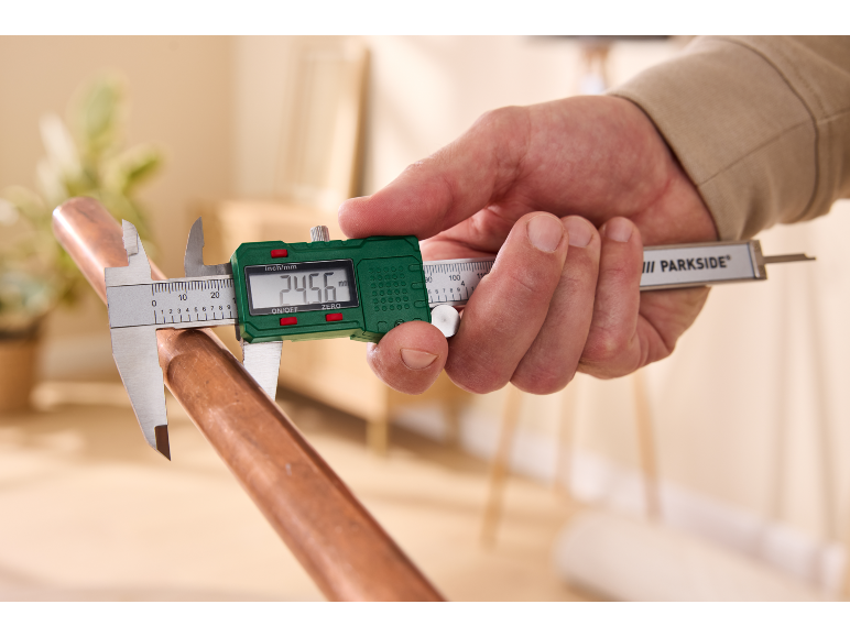 Een man gebruikt een Parkside digitale schuifmaat om een koperen buis te meten.
