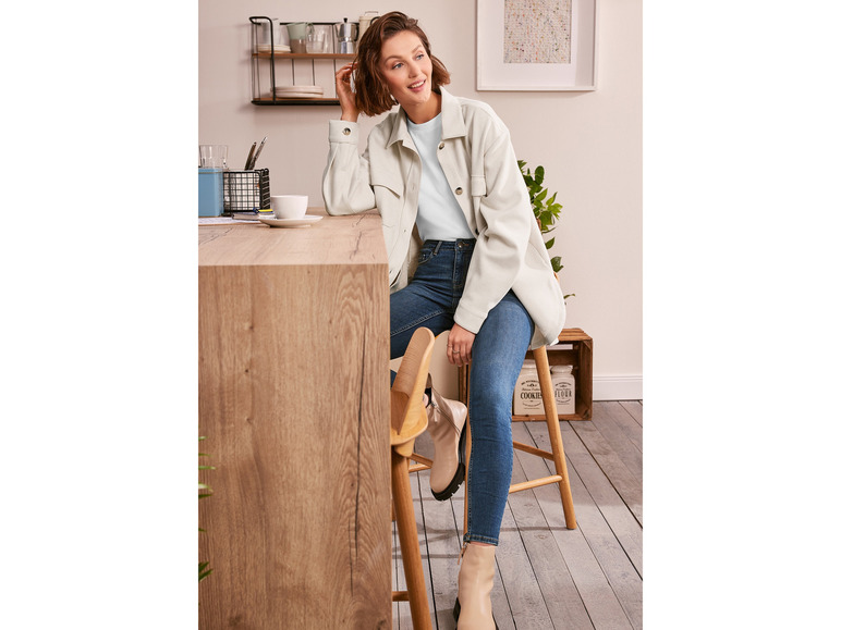 Een vrouw draagt een lichtblauw T-shirt, een witte jas en blauwe skinny jeans.