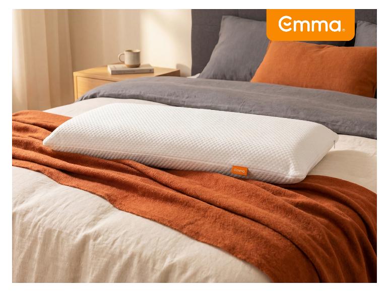 Wit getextureerd kussen op een oranje deken en grijs beddengoed in een slaapkamer