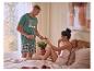 Man in geruite pyjama en 'Sunday Mood' T-shirt biedt fruit aan vrouw in bed.