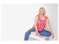 Vrouw in roze top met palmprint en blauwe jeans, zittend op een witte kubus.