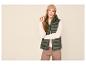 Vrouw in groen gewatteerd vest, beige trui, bruine broek en beige muts.