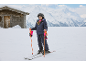 Meisje in ski-jas, skibroek, helm en skihandschoenen op een besneeuwde piste.