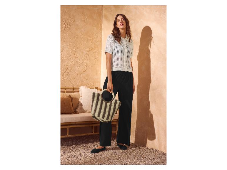 Vrouw in witte gebreide top, zwarte broek en gestreepte handtas in zomerse setting.