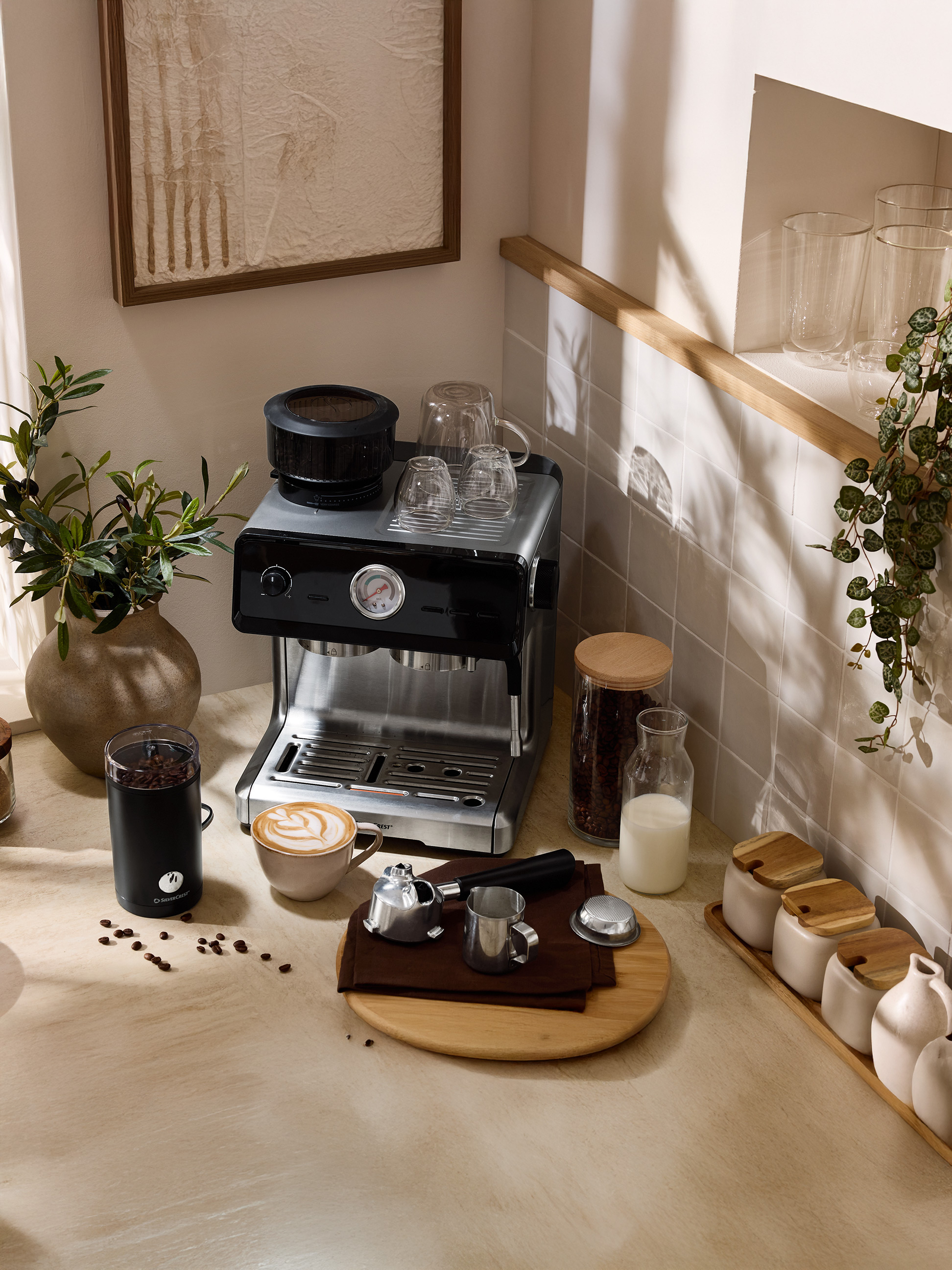 Koffiezetapparaat met molen, latte kopje en accessoires op een aanrecht.