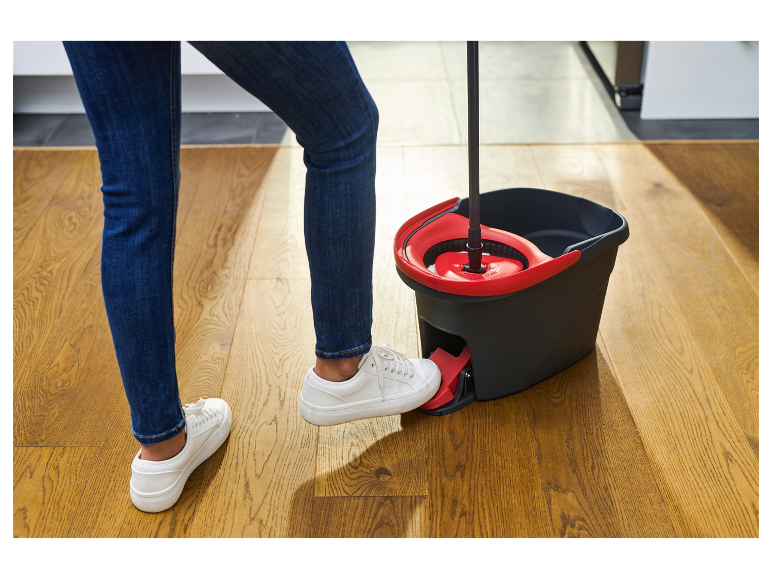 Een vrouw maakt een houten vloer schoon met een emmer en een mop.